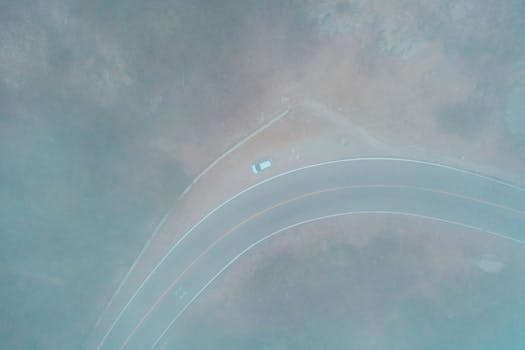 Drone shot of a lone car parked on a foggy curved roadside.