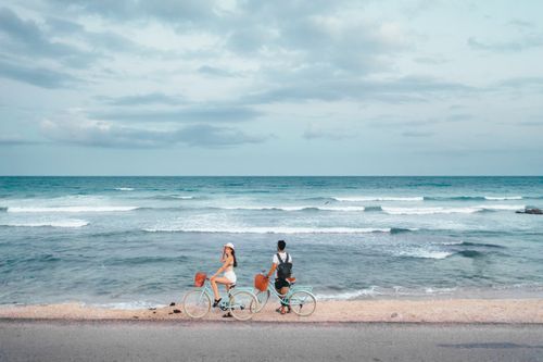 Free Two people cycling by the ocean on a clear day with waves in the background. Stock Photo