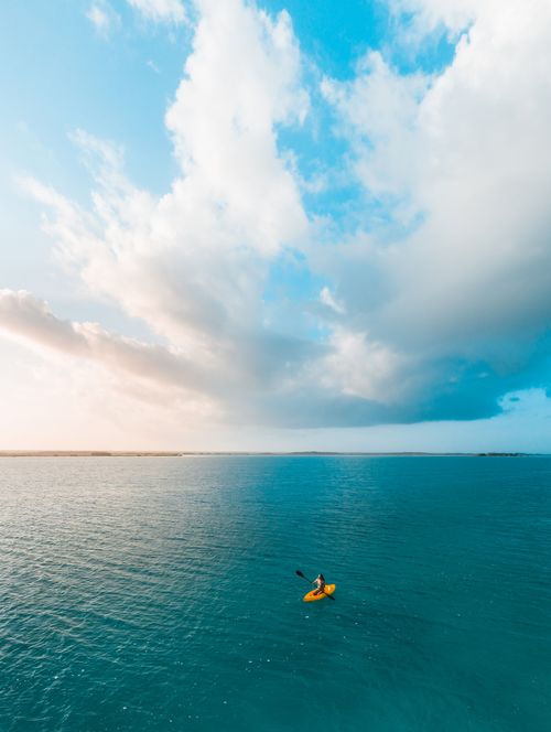 Free A lone kayaker paddles on calm blue waters under a dramatic cloudy sky. Stock Photo