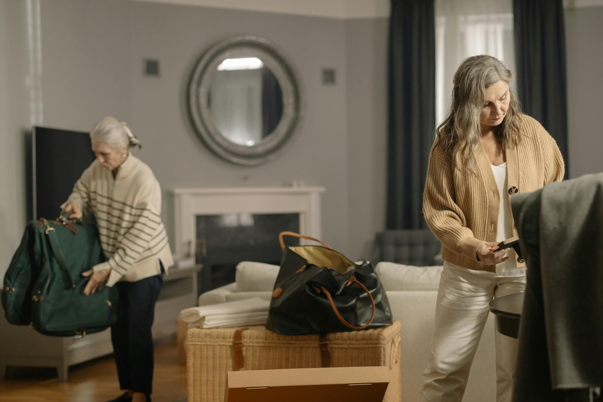 Two senior women packing belongings in a cozy living room setting.