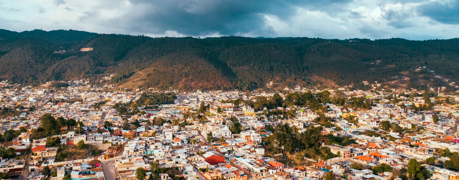 A stunning aerial shot of a vibrant Mexican town against a mountainous backdrop under a cloudy sky.