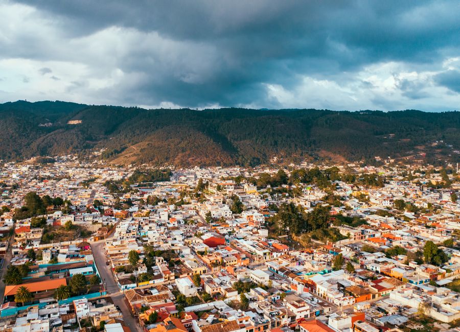 A stunning aerial shot of a vibrant Mexican town against a mountainous backdrop under a cloudy sky.