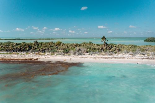 Free A tranquil aerial shot of a serene beach with turquoise waters and lush greenery under a blue sky. Stock Photo
