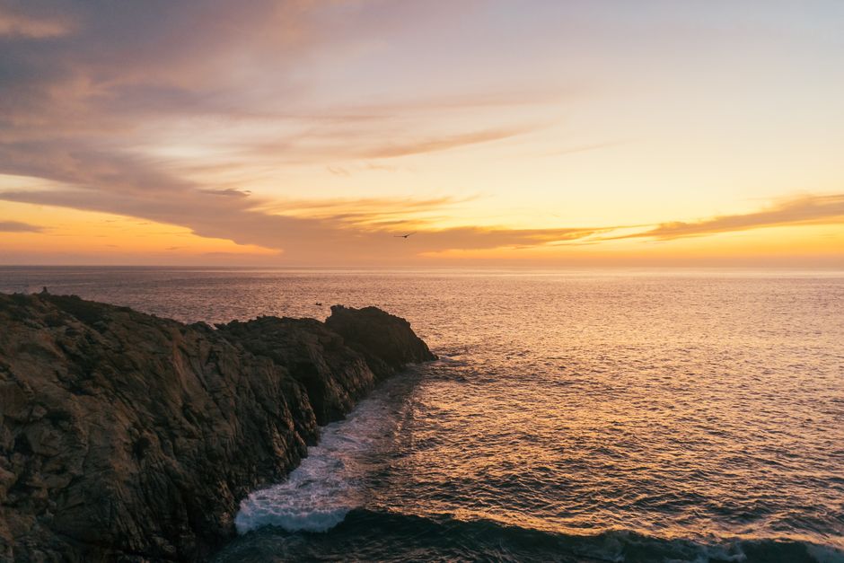 Stunning sunset over a rocky coastline with calm ocean waves, perfect for serene landscape imagery.