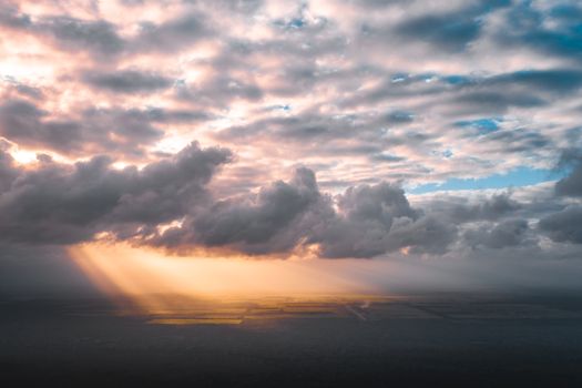 Aerial view of sun rays piercing through clouds, illuminating a tranquil landscape below.