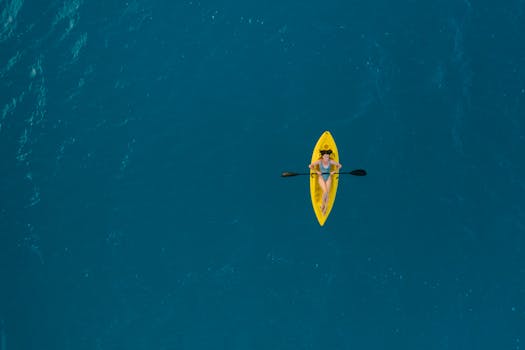 Aerial view of a woman kayaking in the clear, turquoise waters of Bacalar, Mexico.