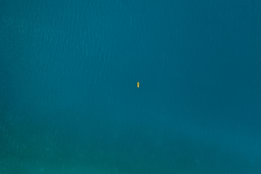 Drone shot of a single kayak in vast blue ocean, showcasing serene adventure.
