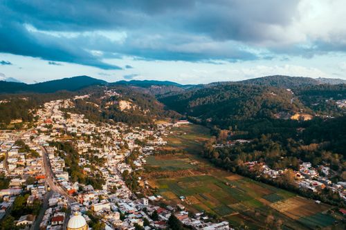 Free Aerial view capturing a rural town nestled against lush green mountains under dramatic skies. Stock Photo