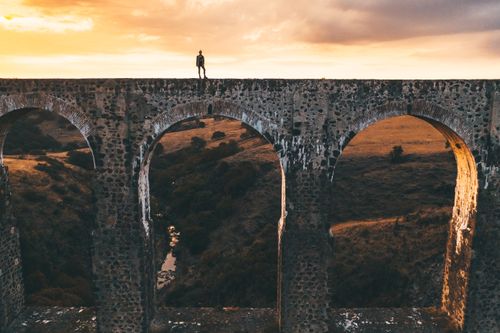 Free A lone person stands on a historic aqueduct during a beautiful sunset, showcasing architectural marvels and scenic landscapes. Stock Photo