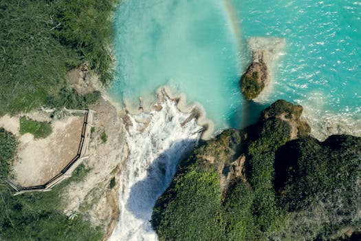 A stunning aerial shot capturing a waterfall flowing into turquoise waters with lush greenery around, creating a serene scene.
