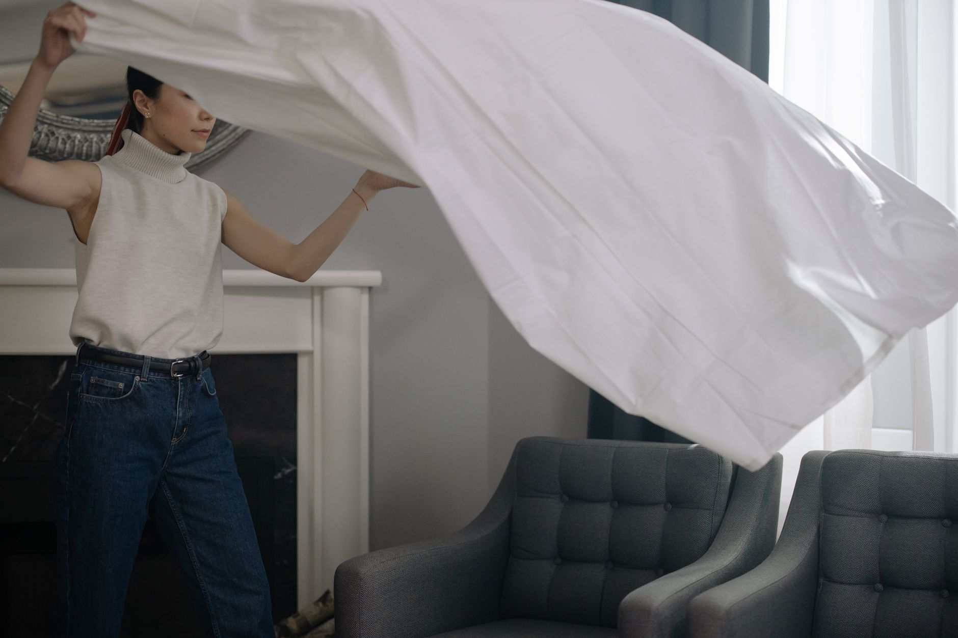 An Asian woman shakes out a white sheet indoors, showcasing modern lifestyle and fashion.