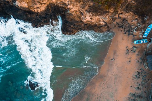 Free A stunning aerial view of a rocky coastline with crashing waves and moored boats on a sandy beach. Stock Photo