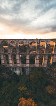 A breathtaking aerial shot of an ancient aqueduct amidst lush greenery during sunset.