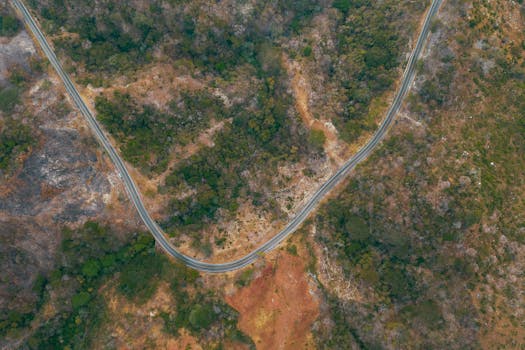 Aerial view showcasing a winding road cutting through a picturesque, natural landscape with diverse vegetation.