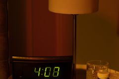 A warm and moody bedside table with a digital clock showing 4:08 and a lamp in dim lighting.