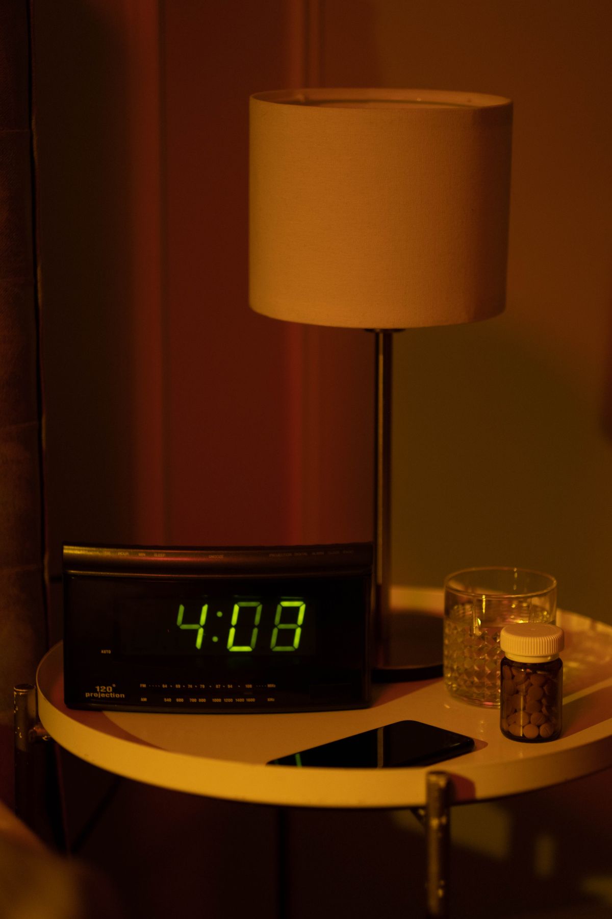 A warmly lit bedside table at night with a digital clock and a small bottle of supplements, illustrating melatonin timing.