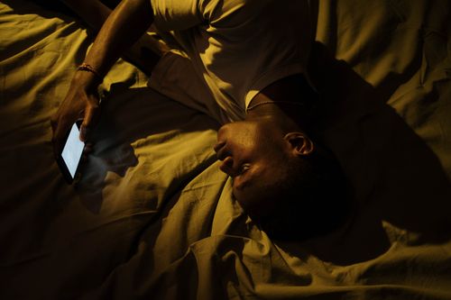 Free A man lying in bed at night, illuminated by a smartphone, suggesting insomnia or sleeplessness. Stock Photo