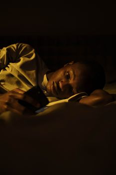 A young man lying in bed at night, illuminated by smartphone screen, creating a moody atmosphere.