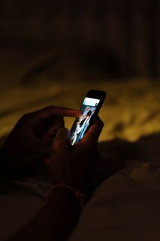 Silhouette of hands holding a lit smartphone in a dark room, close-up view.