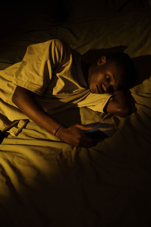 Free A young man lying in bed at night checking his phone, reflecting insomnia and sleeplessness. Stock Photo