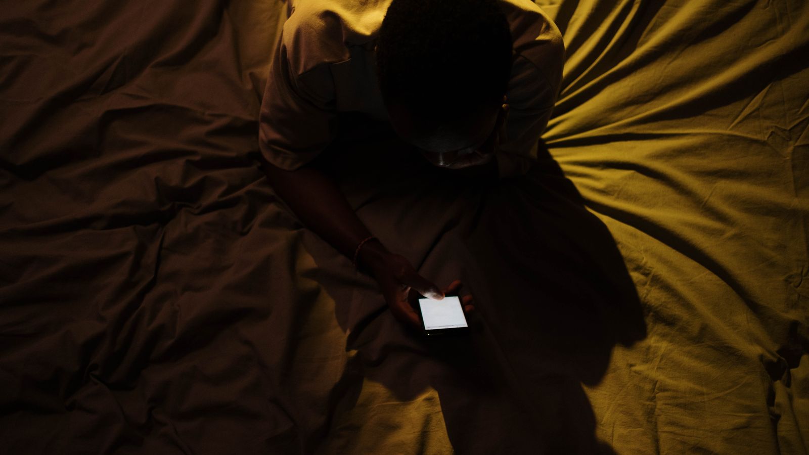 A person lying in bed at night looking at a smartphone, viewed from above