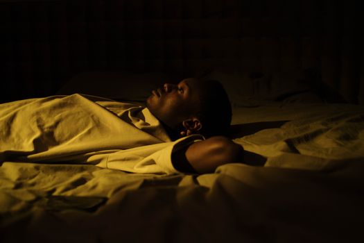 A man struggles with insomnia, lying awake in his dark bedroom at night, reflecting on mental health.