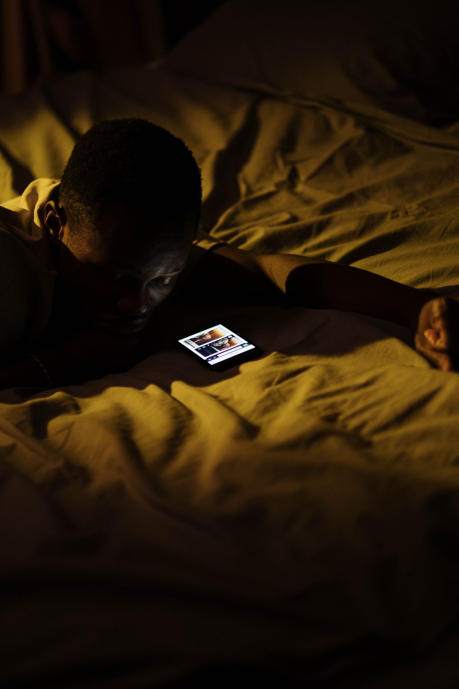 A man lying in bed at night, engaged with his smartphone