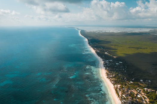 A breathtaking aerial panorama of Tulum's turquoise waters and lush coastline under a bright sky.