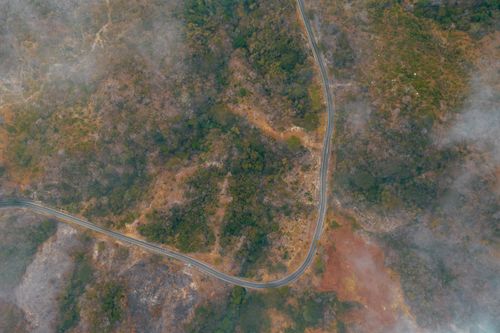 Free A top view of a winding road through dense woodland shrouded in fog, captured from above. Stock Photo
