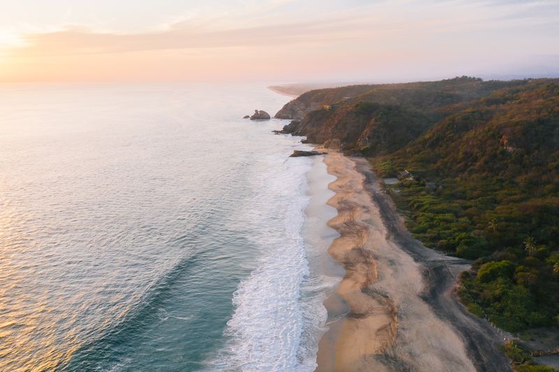 Aerial view of the Oaxaca coastline with dramatic cliffs and surf at sunset