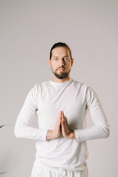 Adult man in white performing a yoga pose indoors with a meditative expression.