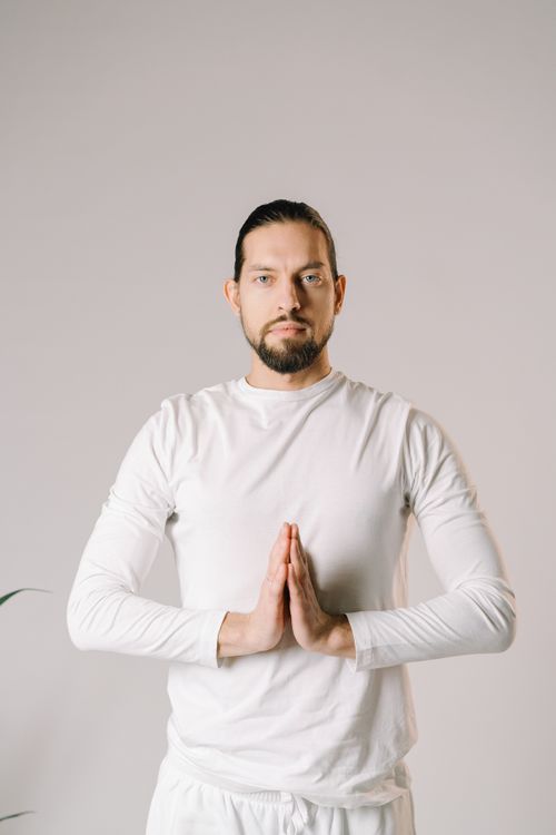 Free Adult man in white performing a yoga pose indoors with a meditative expression. Stock Photo
