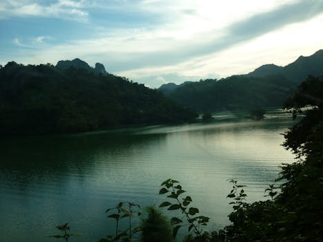 在阴云密布的天空下，宁静的河流被郁郁葱葱的森林和群山环抱