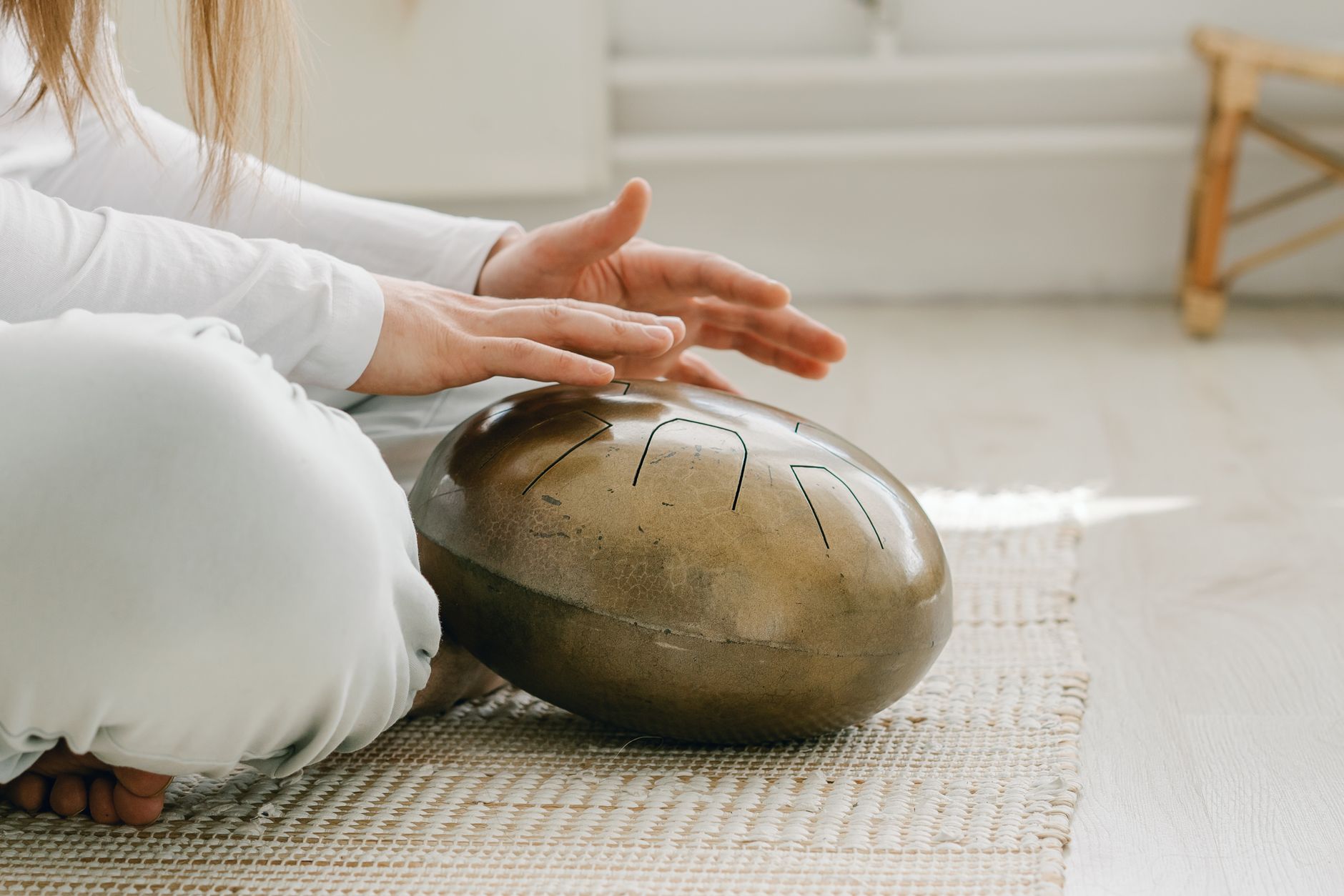 A close-up of hands gently tapping a tongue drum indoors, creating soothing percussion sounds.