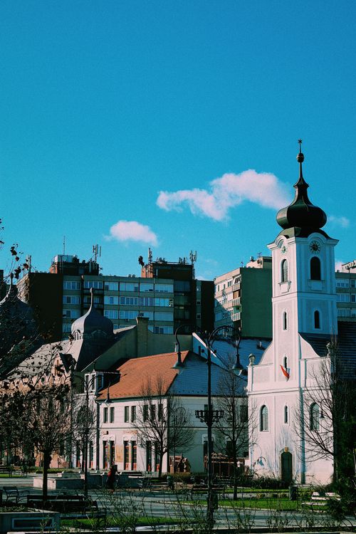 Free Picturesque view of a historic church with modern buildings in Gödöllő, Hungary under clear skies. Stock Photo