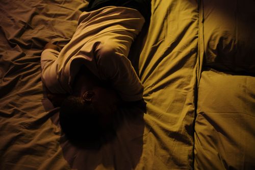 Free A man in white shirt lying on bed in a dimly lit room, displaying tranquility. Stock Photo