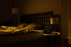 Relaxing dimly lit bedroom with an unmade bed, digital clock displaying 4:12, and warm ambient lighting.