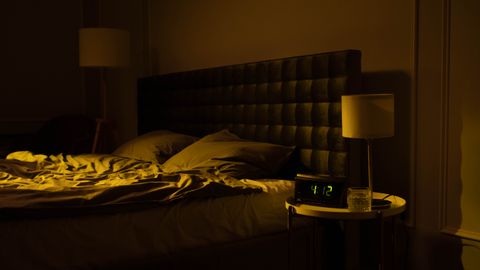 Relaxing dimly lit bedroom with an unmade bed, digital clock displaying 4:12, and warm ambient lighting.