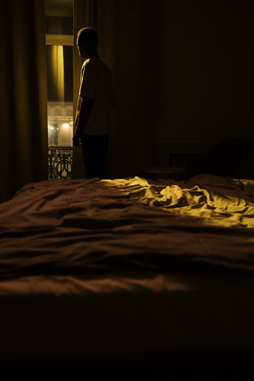 Silhouette of Person Standing by Window in Bedroom at Night