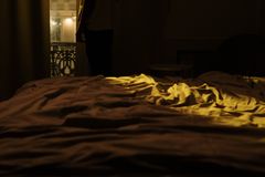 Person standing in a dimly lit bedroom, gazing out the window, capturing a sense of insomnia and solitude.