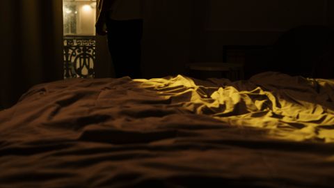 Person standing in a dimly lit bedroom, gazing out the window, capturing a sense of insomnia and solitude.