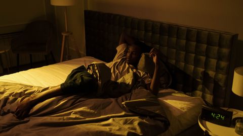 A restless man lying awake on his bed in a dimly lit bedroom at night.
