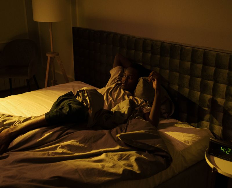 A person struggling to sleep due to pain in a dimly lit bedroom