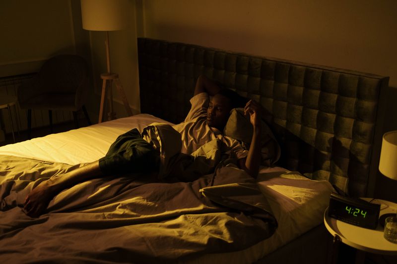 Black African man lying awake in bed at night – insomnia and sleep problems Nigeria