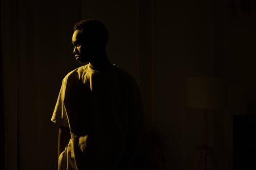 Silhouetted adult man standing indoors, embodying introspection and solitude at night.