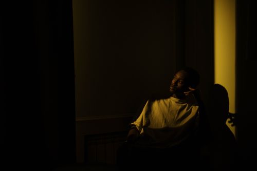 Free A man sits in a dark room with beams of light, evoking introspection and moodiness. Stock Photo