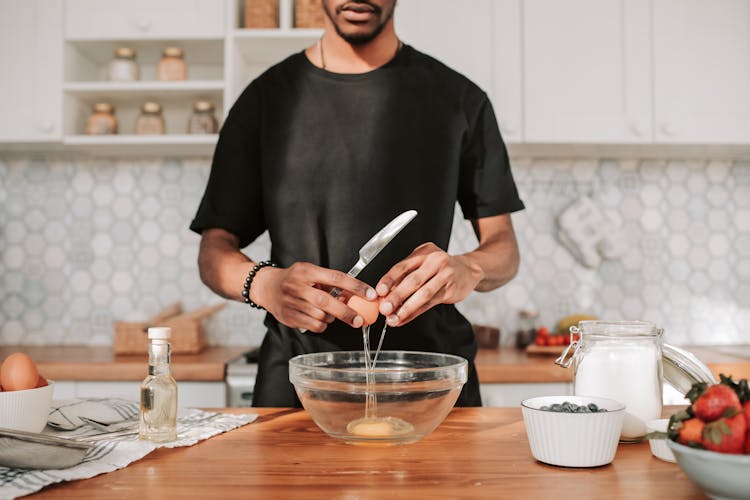 
A Man In A Black Shirt Cracking An Egg