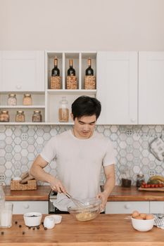 Asian man whisking ingredients in a stylish modern kitchen with jars and bottles.