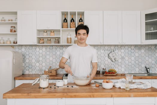Asian man whisking batter in a stylish kitchen setting.