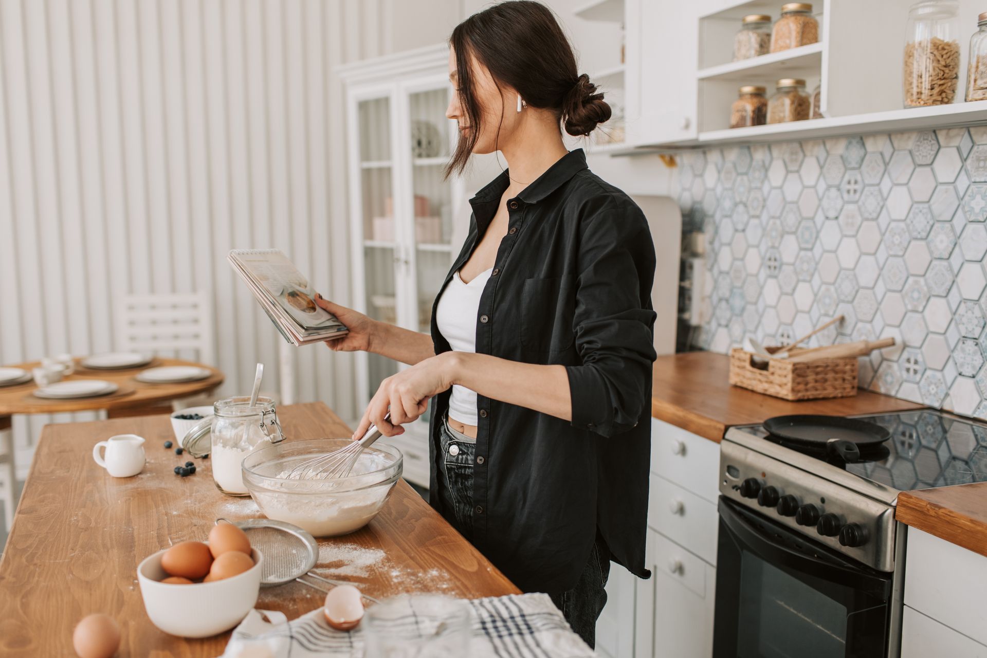 Woman in Black Long Sleeves Holding a Recipe Book While Cooking